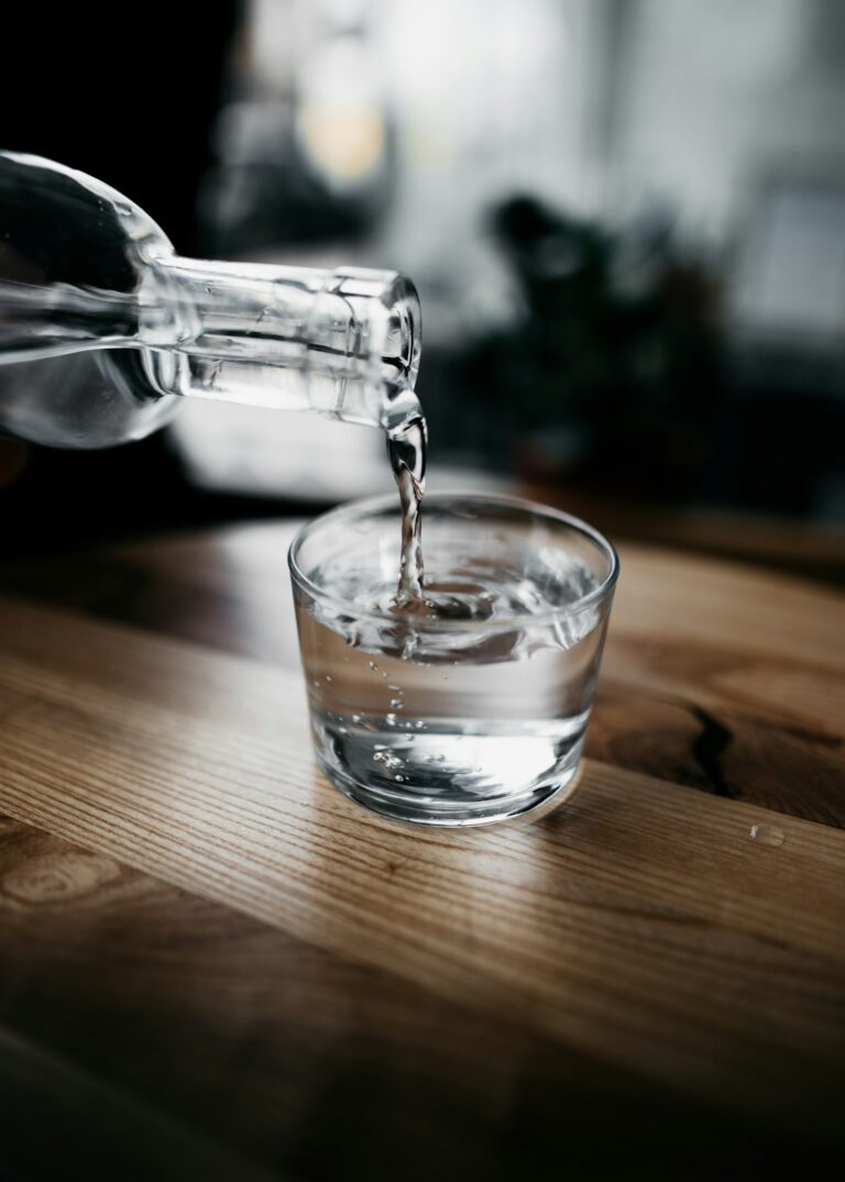 A family filling glasses from a kitchen faucet and unpacking a case of bottled water on the counter.