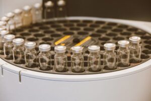 Technician collects a drinking water sample from a kitchen faucet beside a labeled laboratory container.