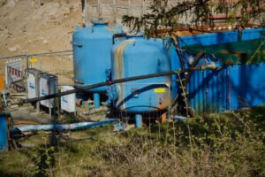 A homeowner checks salt and resin tanks beside household plumbing equipment.